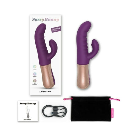 A purple and beige rabbit vibrator with dual stimulation design, displayed alongside its box and a black storage pouch. The product has a curved silicone shaft and a smaller attachment for clitoral stimulation.